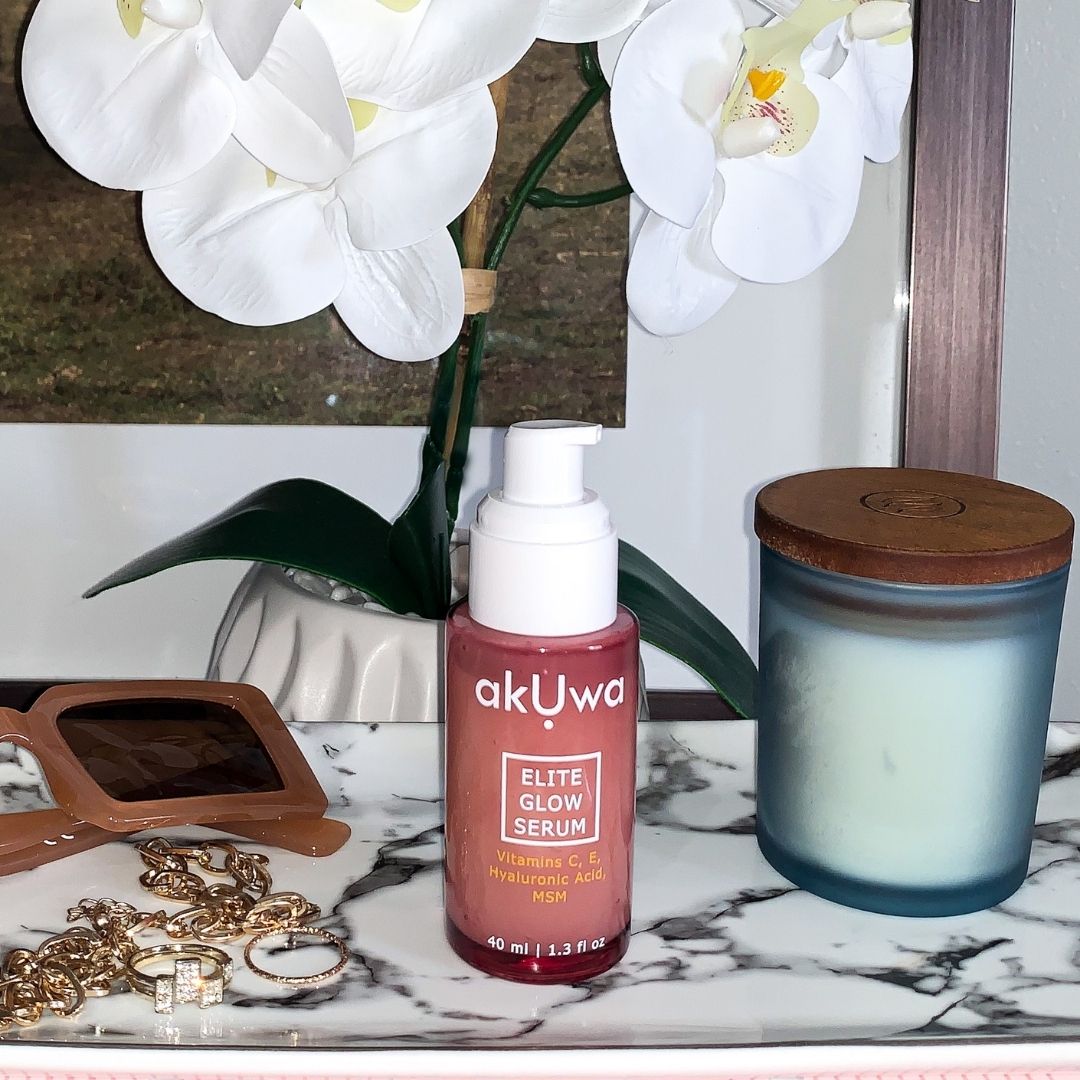 Akuwa serum bottle on marble plate with sunglasses, jewelry, and candle